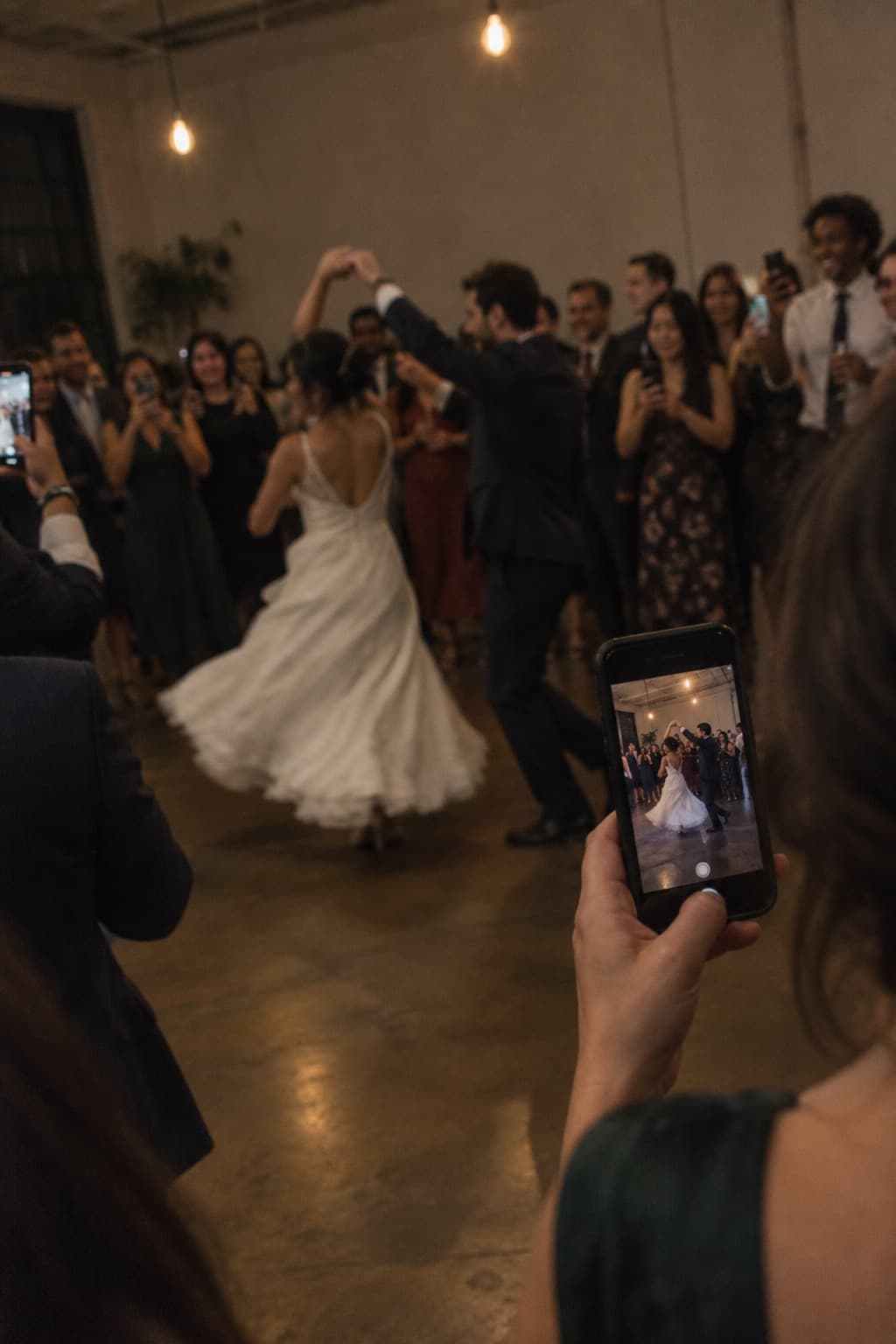A wedding guest filming the couple's first dance on their phone while others do the same